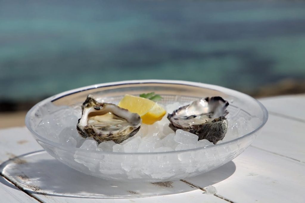 Ostras frescas con limón sobre hielo frente al mar en The Beach